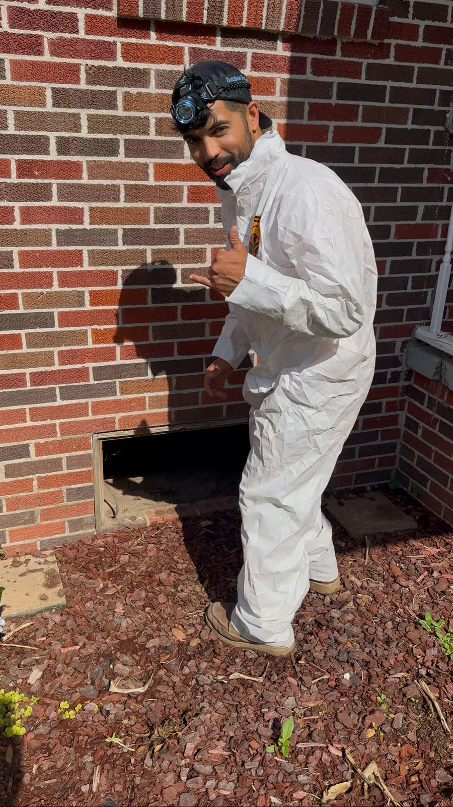 A Wingate's technician in protective coveralls at the crawlspace of an older brick home