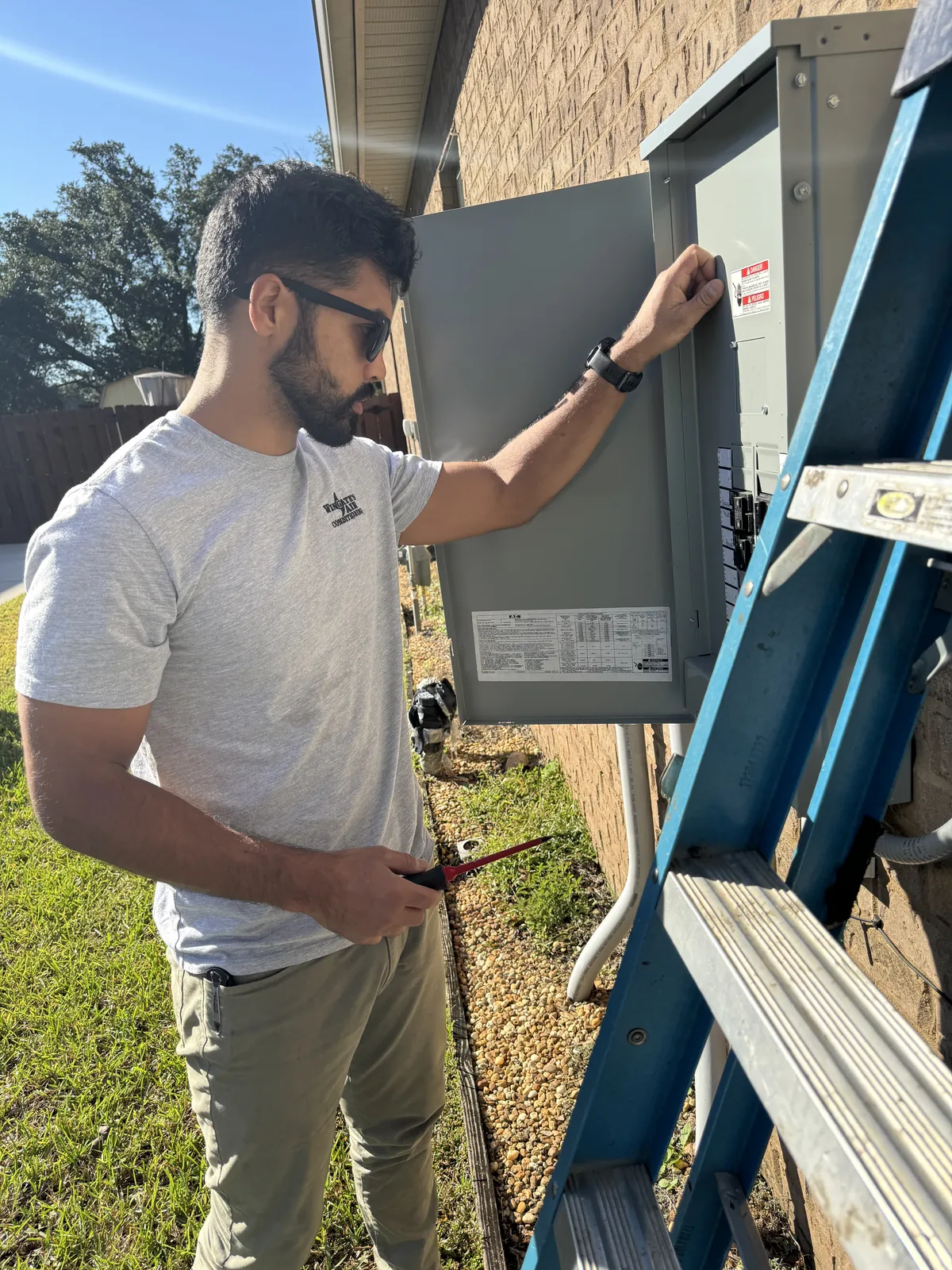 A Wingate's technician opening the outdoor electrical disconnect beside a home