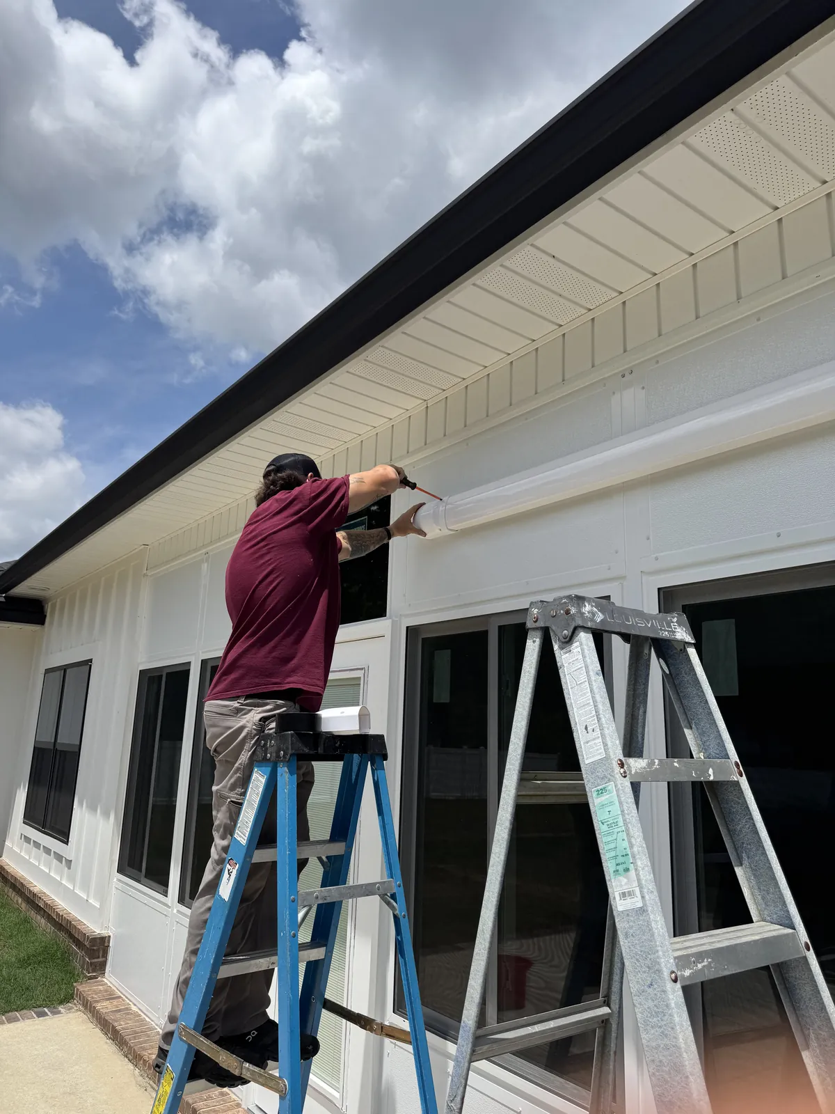 A Wingate's technician on a ladder sealing along the soffit of a home