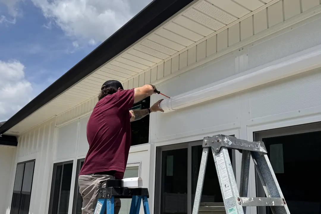 A Wingate's Air Conditioning technician on a ladder working on the exterior of a home near Gulf Breeze, FL