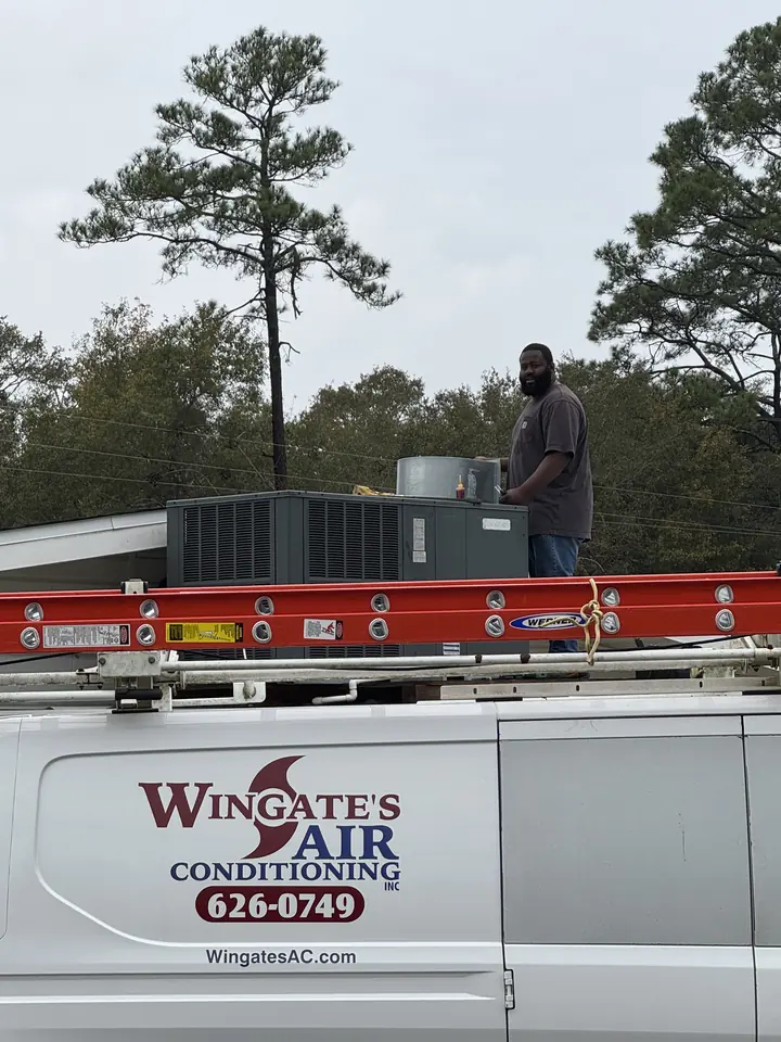 A Wingate's Air Conditioning van parked at a job while a technician works on a rooftop unit near Bagdad, FL