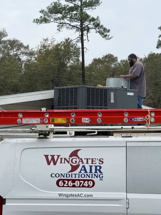 A Wingate's Air Conditioning van with a ladder rack while a technician works on a rooftop unit in Milton, FL