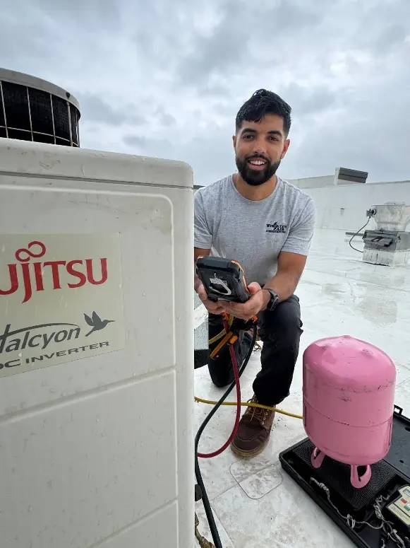 A Wingate's Air Conditioning technician beside a rooftop mini-split condenser near Navarre, FL